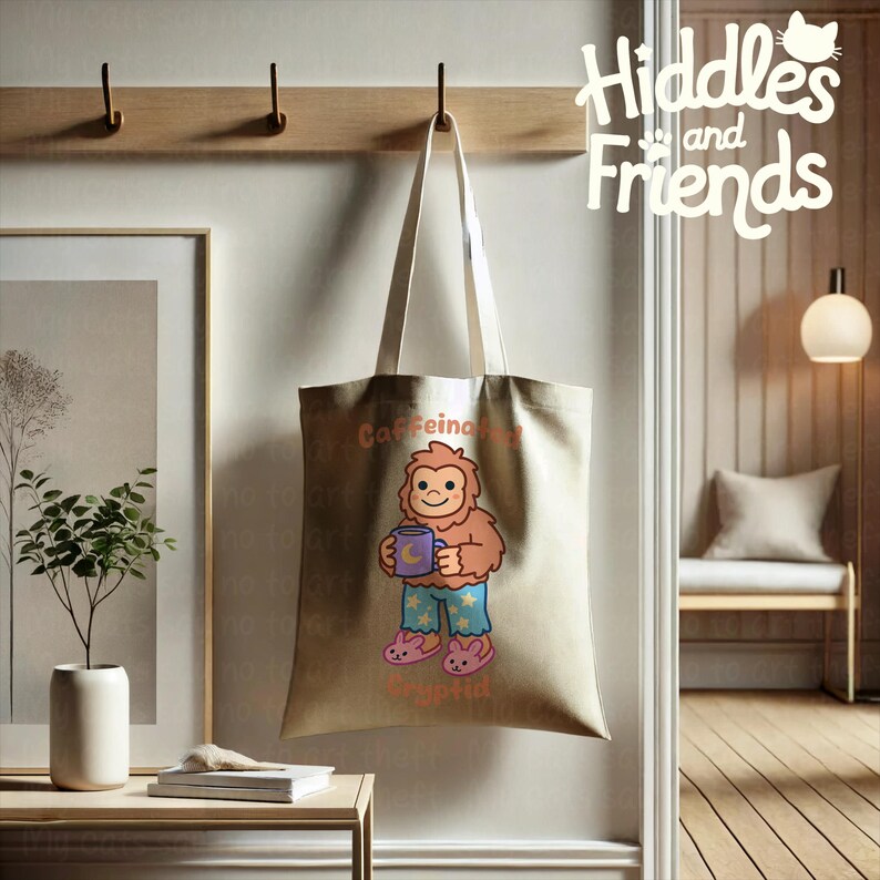 May include: A beige tote bag with a cartoon illustration of a brown Bigfoot wearing blue pajamas with stars and holding a purple mug with a crescent moon. The text "Caffeine and Cryptid" is printed on the bag.