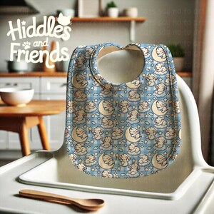 May include: A blue and white baby bib with a pattern of sleeping bunnies on clouds and moons. The bib has a white trim and a large opening for the neck.
