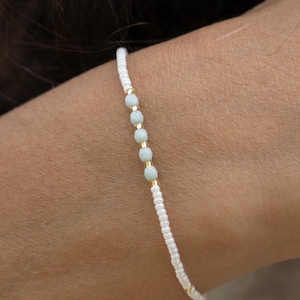 Op de afbeelding: Een delicate witte kralen armband met een enkele rij lichtblauwe kralen.