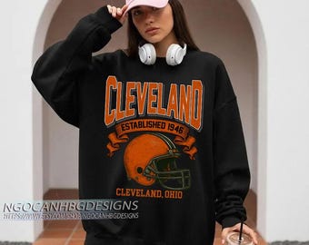 May include: Black sweatshirt with the word "Cleveland" in orange block letters, a football helmet graphic, and the text "Established 1946." The sweatshirt is a classic crew neck style.