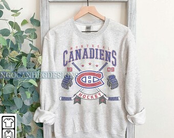 Puede incluir: Una sudadera gris con un gráfico de estilo vintage del logotipo del equipo de hockey de los Canadiens de Montreal. El gráfico incluye el nombre del equipo, "Canadiens", los años "1909" y "Hockey".