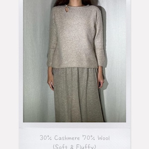 Può includere: Un completo in maglia beige composto da 30% cashmere e 70% lana. Il maglione a maniche lunghe ha un dettaglio a forma di buco della serratura sullo scollo. La gonna abbinata è lunga fino al ginocchio. Il testo sull'immagine recita "30% Cashmere 70% Wool (Soft & Fluffy)".