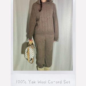May include: A brown knit co-ord set consisting of a hooded long-sleeve sweater with vertical cable knit detailing and matching trousers. The set is labeled 100% Yak Wool Co-ord Set. A white and gray checkered handbag with tan leather handles is included.