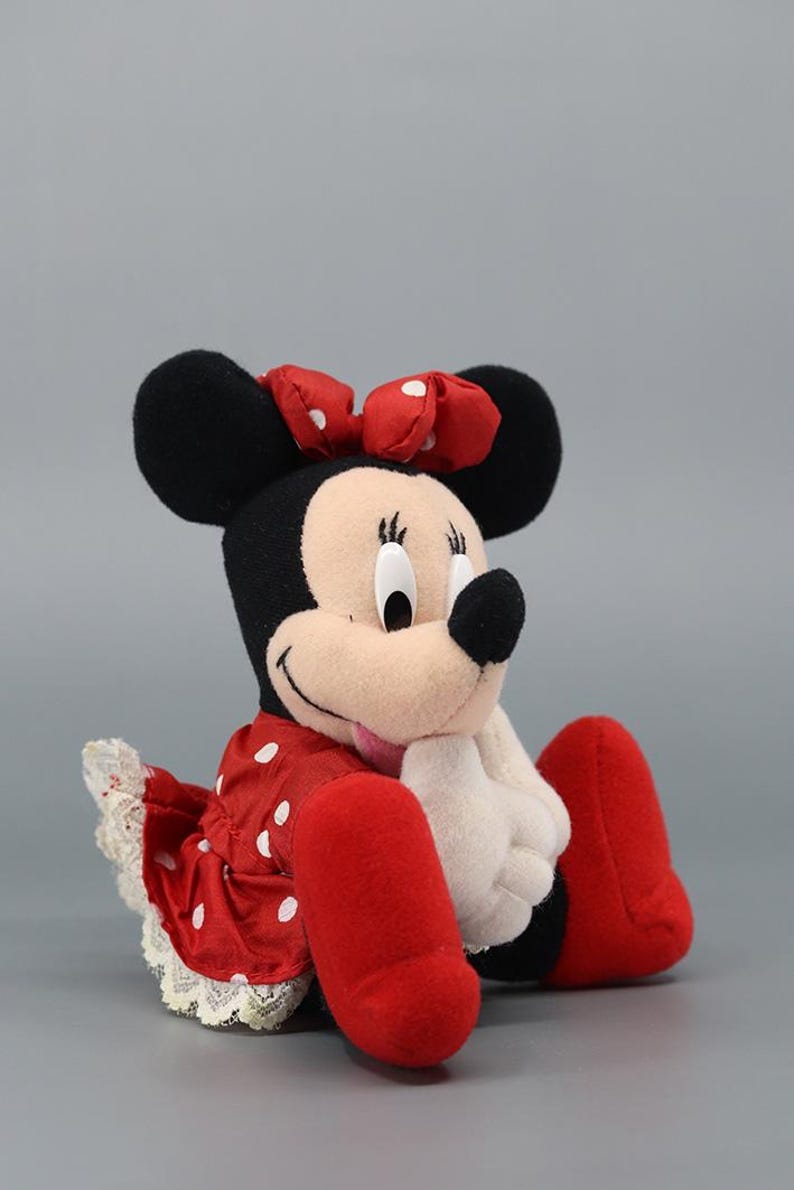 May include: A plush Minnie Mouse doll, featuring black ears, a red polka-dot dress, and a matching bow. The doll has white gloves and red shoes. The overall design is a classic representation of the iconic cartoon character.