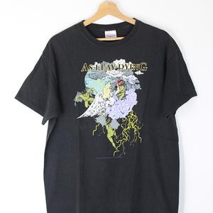 May include: Black t-shirt with a graphic print of a winged figure surrounded by clouds and lightning. The text "As I Lay Dying" is printed in gold above the graphic.