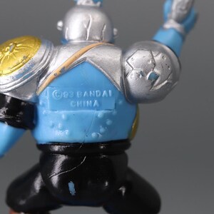 May include: A blue and silver action figure with gold accents. The figure has a helmet, shoulder pads, and black pants. The text "&copy;93 BANDAI CHINA" is visible on the back.