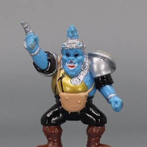 May include: A blue action figure with a silver helmet and shoulder pads, black pants, and brown boots. The figure has a gold chest and a tan satchel. It is holding a silver weapon and standing on a blue base.