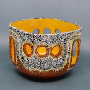 May include: A decorative ceramic bowl with a speckled gray exterior, featuring orange and yellow accents. The bowl has a geometric design with circular cutouts and a bright yellow interior. The rim is also yellow.