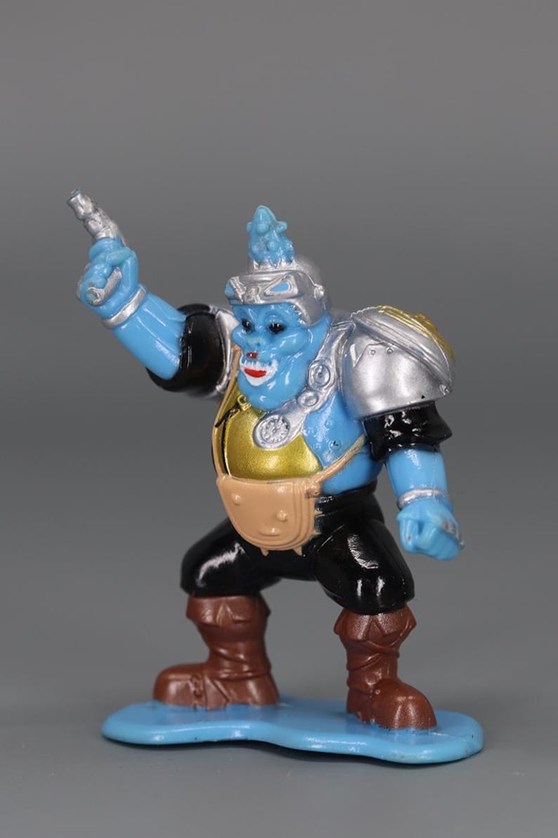 May include: A blue action figure with silver armor, a gold chest, and a brown satchel. The figure is holding a silver gun and is wearing black pants and brown boots. It stands on a blue base.