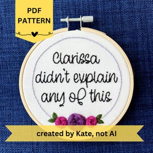 May include: A white fabric embroidery hoop with the text "Clarissa didn't explain any of this" in black thread. The design includes embroidered pink and purple flowers. The text "PDF PATTERN" and "created by Kate, not AI" are also present.