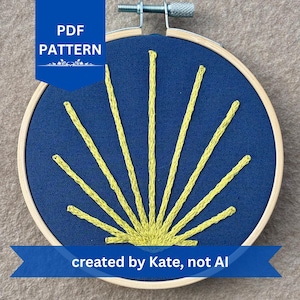 May include: A blue fabric embroidery hoop with a yellow sunburst design. The text "PDF PATTERN" is in a blue banner at the top, and "created by Kate, not AI" is in a blue banner at the bottom. The hoop is made of wood.