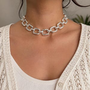 May include: A shiny silver-toned choker necklace featuring a series of thick, rounded rectangular links connected in a continuous chain pattern. The metallic links have a smooth, polished finish that reflects light, creating a bold, uniform appearance.