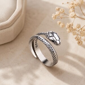 May include: A silver-toned open ring shaped like a coiled snake with textured scales and a smooth head. The inner band is clearly stamped with the text S925, indicating the metal composition. The design features a gap, allowing for adjustment.