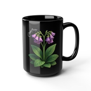 May include: Black ceramic mug featuring a Comfrey plant illustration. The design includes a Comfrey plant with purple bell-shaped flowers and green leaves. The word "Comfrey" is written in a cursive font.