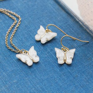 May include: A gold chain necklace and a pair of earrings with white butterfly charms. The butterfly charms have a sparkly, iridescent finish.