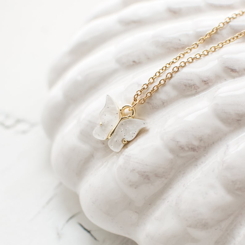 May include: A delicate gold chain necklace with a white sparkly butterfly pendant.