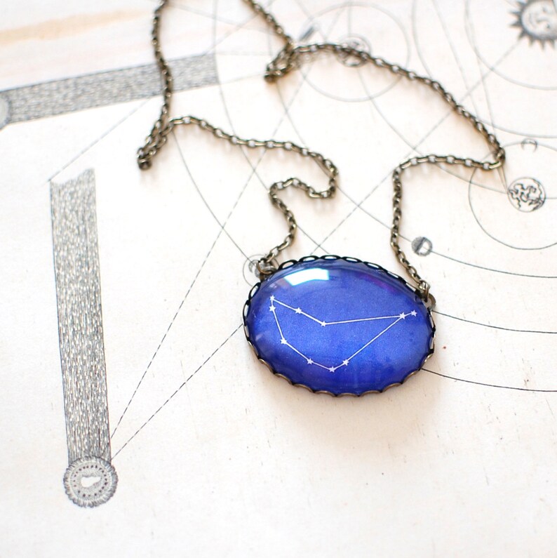 May include: A blue glass pendant necklace with a silver chain. The pendant features a white outline of the constellation Capricorn.