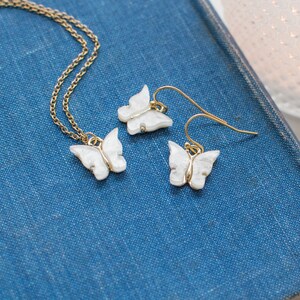 May include: A set of delicate gold butterfly earrings and a matching necklace. The butterflies are white with a sparkly finish.