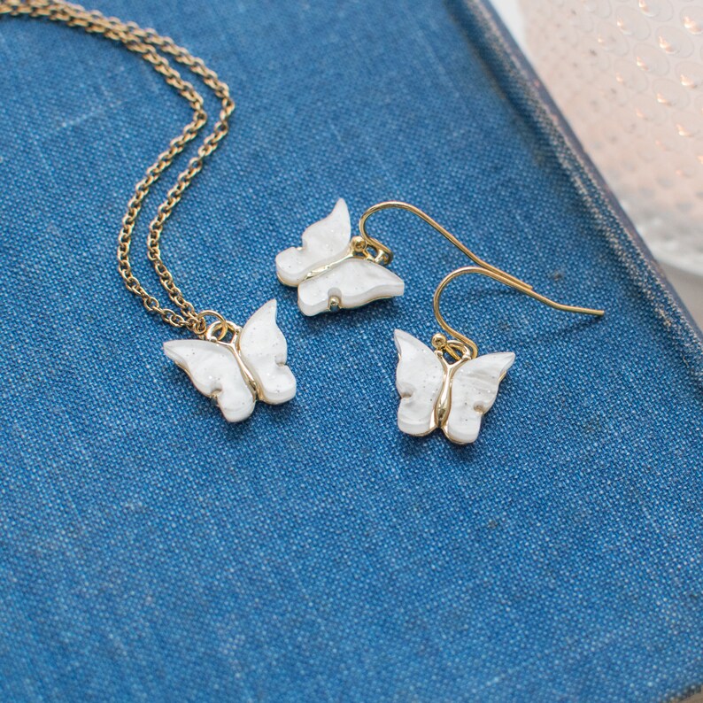 May include: A set of delicate gold butterfly earrings and a matching necklace. The butterflies are white with a sparkly finish.