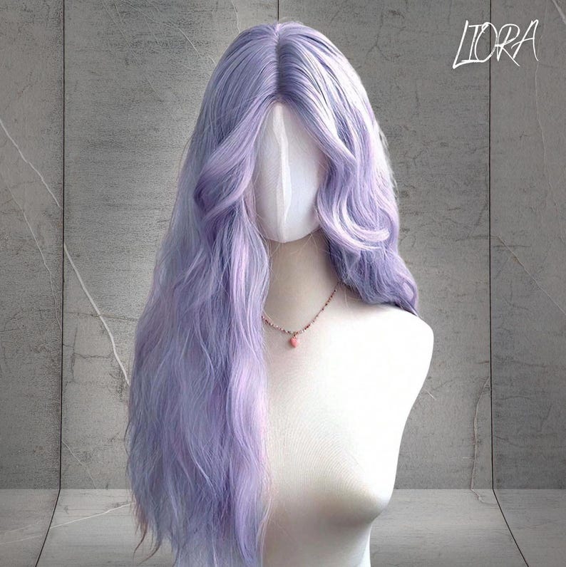 May include: A long, wavy lavender wig displayed on a mannequin head. The wig features a natural-looking hairline and soft, flowing curls. A delicate necklace with a pink pendant adorns the mannequin's neck. The word "LIORA" is written in cursive in the top right corner.