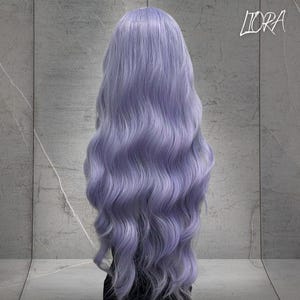 May include: A long, wavy wig in a soft lavender hue. The wig features a natural-looking hairline and voluminous, flowing locks. The word "LIORA" is written in cursive in the upper right corner.