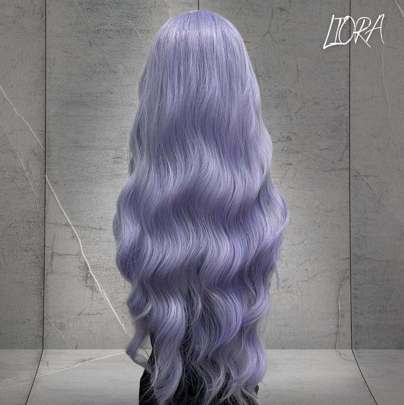 May include: A long, wavy wig in a soft lavender hue. The wig features a natural-looking hairline and voluminous, flowing locks. The word "LIORA" is written in cursive in the upper right corner.