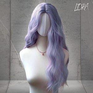 May include: A long, wavy lavender wig styled on a mannequin head. The wig features a natural-looking part and soft, flowing layers. A delicate pink necklace with a pendant adorns the mannequin's neck. The word "LIORA" is written in cursive in the top right corner.