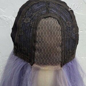 May include: A close-up view of the inside of a wig. The wig cap is black with a mesh center and a light purple lace front. The wig has long, light purple hair.