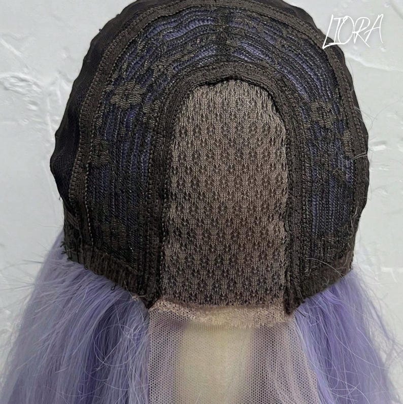 May include: A close-up view of the inside of a wig. The wig cap is black with a mesh center and a light purple lace front. The wig has long, light purple hair.