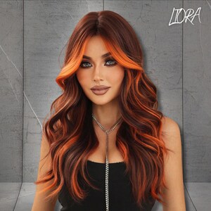May include: A woman with long, wavy auburn hair with bright orange highlights. The hair frames the face, and the woman is wearing a black top and a silver necklace. The word "LIORA" is in the upper right corner.
