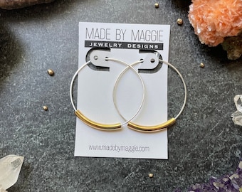May include: Silver hoop earrings with a gold bar accent. The earrings are displayed on a white card with the text "Made by Maggie Jewellery Designs" and "www.madebymaggie.com".