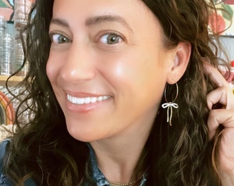 Puede incluir: Una mujer con una camisa vaquera, un collar de cadena de oro y pendientes de aro con un dije de lazo blanco.