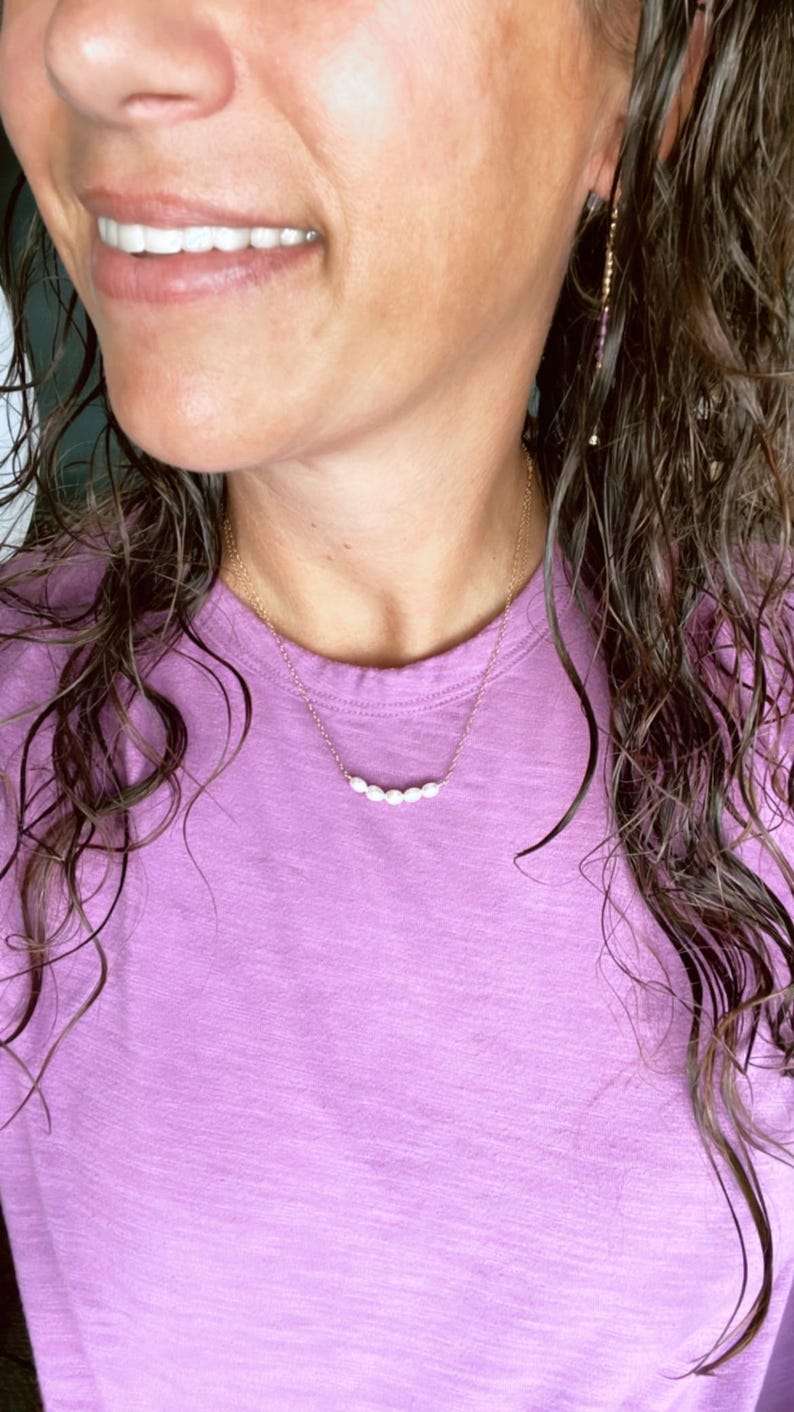 Puede incluir: Una mujer con una camisa morada con un delicado collar de cadena dorada con una fila de peque&ntilde;as perlas blancas.
