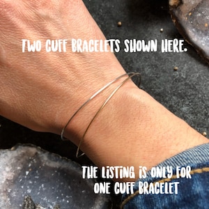 May include: Two thin cuff bracelets, one silver and one gold, are shown on a wrist. The text in the image reads: "TWO CUFF BRACELETS SHOWN HERE." and "THE LISTING IS ONLY FOR ONE CUFF BRACELET."