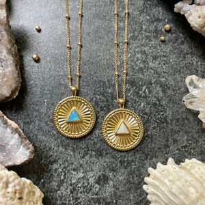 May include: Two gold necklaces with opal triangle pendants. The pendants are set in a circular frame with a sunburst design. The necklaces are on a dark gray background.