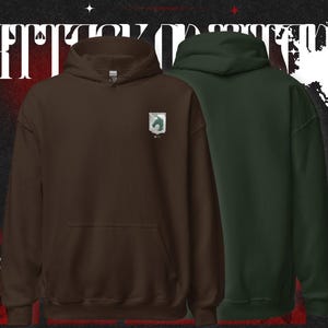 Könnte beinhalten: Zwei Kapuzenpullover, einer braun und einer dunkelgrün, werden vor einem dunklen Hintergrund mit weißem Text und japanischen Schriftzeichen gezeigt. Der braune Hoodie hat ein kleines Emblem auf der Brust. Beide haben eine Vordertasche und eine Kapuze.