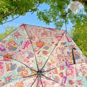 Puede incluir: Un paraguas rosa y blanco con un patrón colorido de personajes de dibujos animados y texto. El texto incluye "ADMIT ONE", "Hearbrucker", "BUFF" y "80".