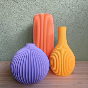 Może przedstawiać: Trzy ceramiczne wazony z żebrowanym wzorem. Wazony są w odcieniach pomarańczowego, żółtego i fioletowego.