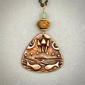 Pode incluir: Um colar com um pingente de cobre em forma de triângulo que apresenta dois peixes e um grupo de cogumelos. O pingente está preso a uma conta verde e marrom e uma corrente dourada.
