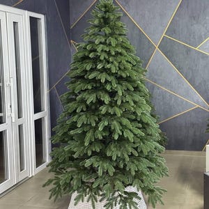 Könnte beinhalten: Ein üppiger, grüner künstlicher Weihnachtsbaum mit dichtem Nadelwerk steht in einem weißen, gewebten Korb. Der Hintergrund ist eine dunkelgraue Wand mit goldenen geometrischen Akzenten. Eine festliche Dekoration.