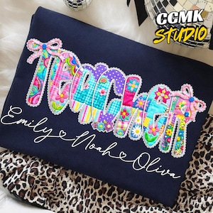 Pode incluir: Camisola azul marinho com a palavra "TEACHER" num design de patchwork colorido. Os nomes "Emily", "Noah" e "Oliva" estão escritos em itálico por baixo. A camisola está sobre um tecido com estampa de leopardo.