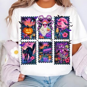 May include: A white t-shirt featuring a graphic print of six rectangular postage stamp designs. The illustrations include a jack-o'-lantern, a ghost wearing heart-shaped sunglasses, a full moon, a black cat, a pool scene labeled SUMMERWEEN, and a skeleton hand holding a cocktail glass.