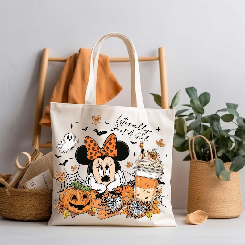 Pu&ograve; includere: Una borsa in tela color crema con una stampa grafica di un topo dei cartoni animati con un fiocco a pois, una zucca, una ragnatela e una tazza di caff&egrave;. Il testo "Literally Just A Girl" &egrave; stampato in nero sopra l'illustrazione.