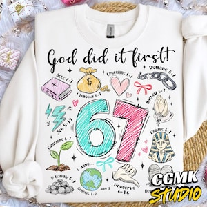Puede incluir: Sudadera blanca con la frase "God did it first!" y el número "67" en turquesa y rosa. El diseño incluye ilustraciones y versículos bíblicos, ideal para ropa cristiana.