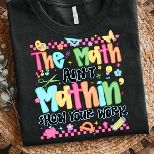 May include: Black t-shirt with a colorful graphic that reads "The Math Ain't Mathin' Show Your Work." The design includes math symbols, a butterfly, flowers, and a pencil. The text is in various bright colors.