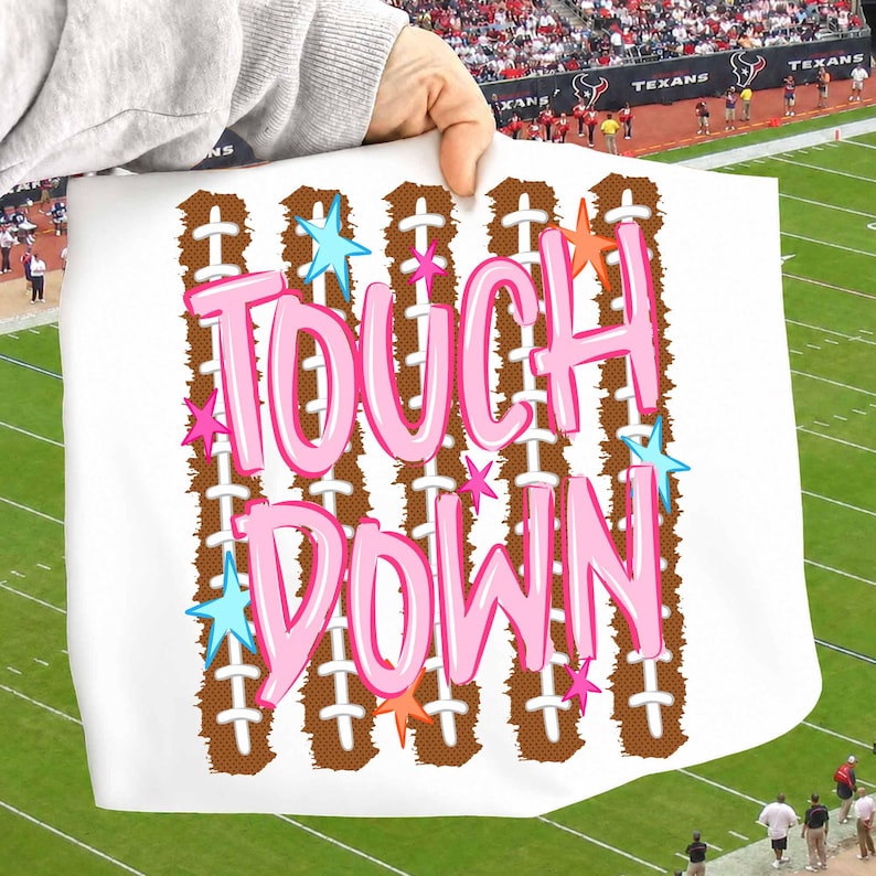 May include: A white rectangular sign featuring the text TOUCH DOWN in large pink bubble letters. The background design consists of vertical brown football patterns with white laces, accented by small light blue, pink, and orange stars.