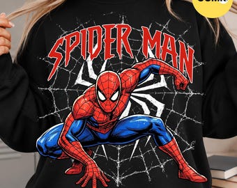 May include: A black crewneck sweatshirt featuring a graphic of the character Spider-Man in a crouching pose. The design includes a white spiderweb background and the text SPIDER MAN in bold red letters across the top of the chest area.