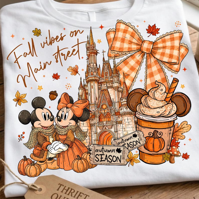 Puede incluir: Una camiseta blanca con un estampado gr&aacute;fico que incluye el texto Fall vibes on Main street, un castillo, dos ratones de dibujos animados con ropa de oto&ntilde;o, un lazo grande a cuadros naranja, una bebida de calabaza y dos tickets autumn SEASON.