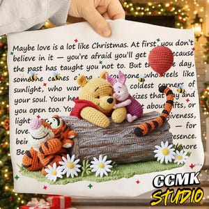 May include: A crocheted Winnie the Pooh, Piglet, and Tigger scene on a log, with a red balloon and bees. The background includes text that reads "Maybe love is a lot like Christmas." The image is held by a hand.