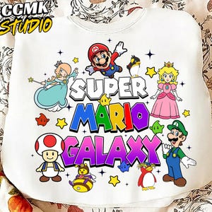 May include: White sweatshirt featuring a colorful Super Mario Galaxy graphic. The design includes Mario, Princess Peach, Luigi, and other characters. The text "CCMK STUDIO" is in the upper left corner.